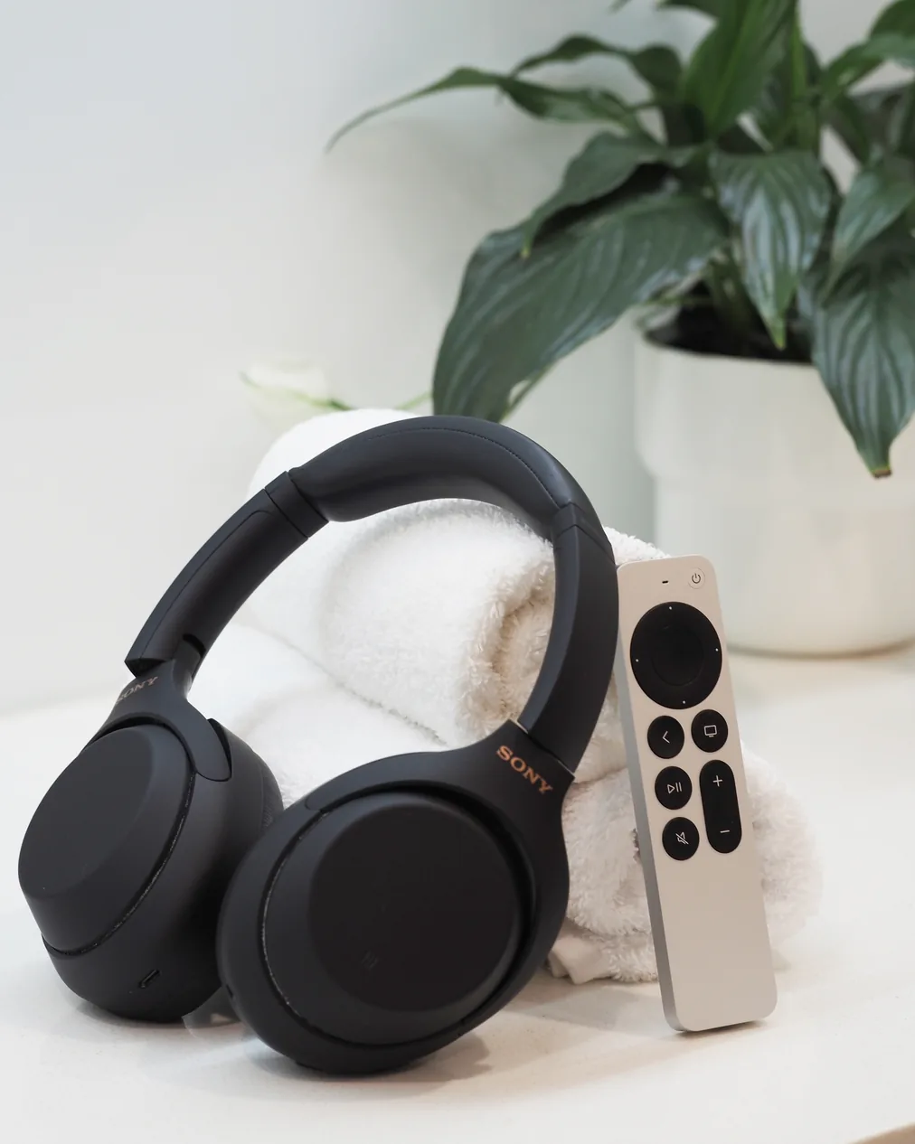 Noise-cancelling headphones and an Apple TV remote resting on a folded towel beside a potted plant in the practice.