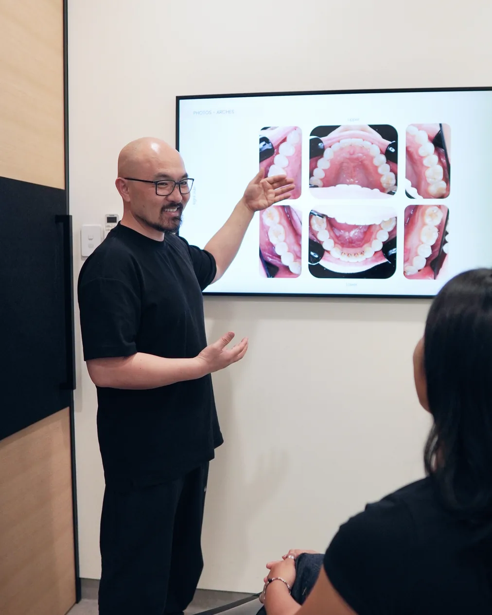 A Kin Dental Studio dentist standing at a wall screen of intraoral scan photos, talking a seated patient through the images.